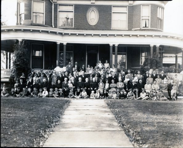 John W. and Cataherine Kleinhenz hold a family reuntion and celebration in their new home at 518 West Jackson Street in St Marys, Ohio, on September 30, 1928 about ten months after moving into the Castle house. 
John W. Kleinhenz is in the middle of the photo, standing, wearing a bow tie.
Catherine Kleinhenz is on John W.'s left, standing.
Hilda Kleinhenz is standing on Catherine's left.
Mabel (Klosterman) Kleinhenz is standing on Hilda's left.
Raymond Kleinhenz is standing on John W.'s left. Behind Catherine.
Alfred Kleinhenz is standing on Raymond's left.
Arnold Kleinhenz is standing on John W.'s right.
Minnie Kleinhenz is in the right half of the photo, sitting, wearing a speckled dress with her arms folded.
Leondard Kleinhenz is standing behind Minnie.
Alfrida Kleinhenz is sitting on Minnie's right.
Likely-Olive (Kleinhenz) Thieman is sitting on Alfrida's right.
Pauline Kleinhenz is standing behind Alfrida.
George Klosterman in sitting with arms folded on Minnie's left.
Mary Ann (Schwieterman) Klosterman is sitting, hands crossed, on George's left.
Father Sebastion Kremer is the middle priest. Sitting.
George Thieman is sitting holding a child next to a priest.
Esther and Edwin Kleinhenz are sitting on the bottom row under the two leftmost priests.
Robert John Kleinhenz, son of Raymond and Mabel, is the little boy on the bottom row at the top of the right sidewalk line wearing a sailor-looking outfit.